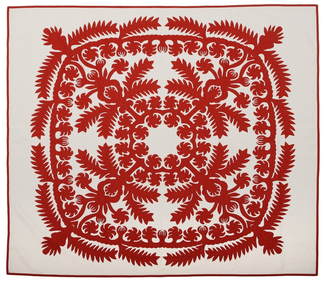 This quilt is asymmetrical with one large red design covering the white background. The design includes diagonal and curvilinear floral designs and shapes. Specifically, pineapples and pineapple leaves.