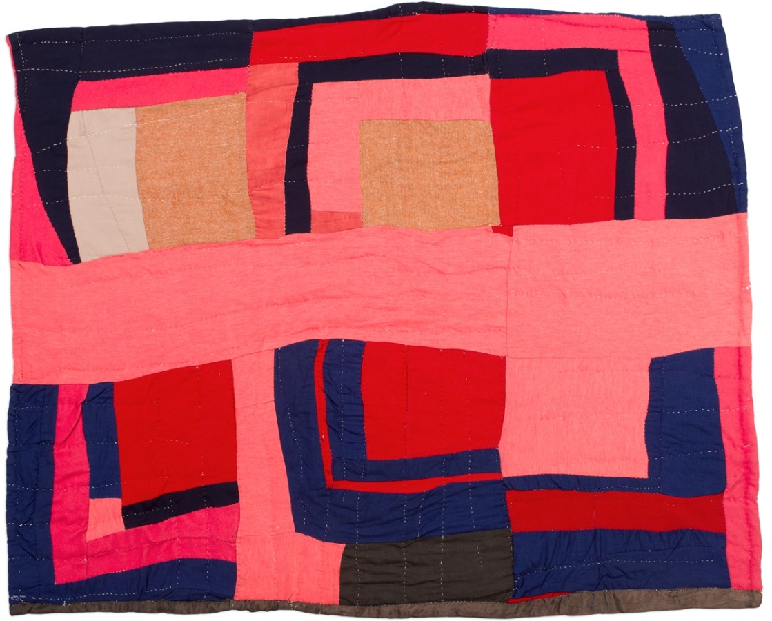 This quilt is asymmetrical with multiple squares and rectangles that vary in size. The rectangles and squares are red, pink, white, light brown, blue and black. There is also a thick pink rectangle running horizontally across the middle of the quilt.
