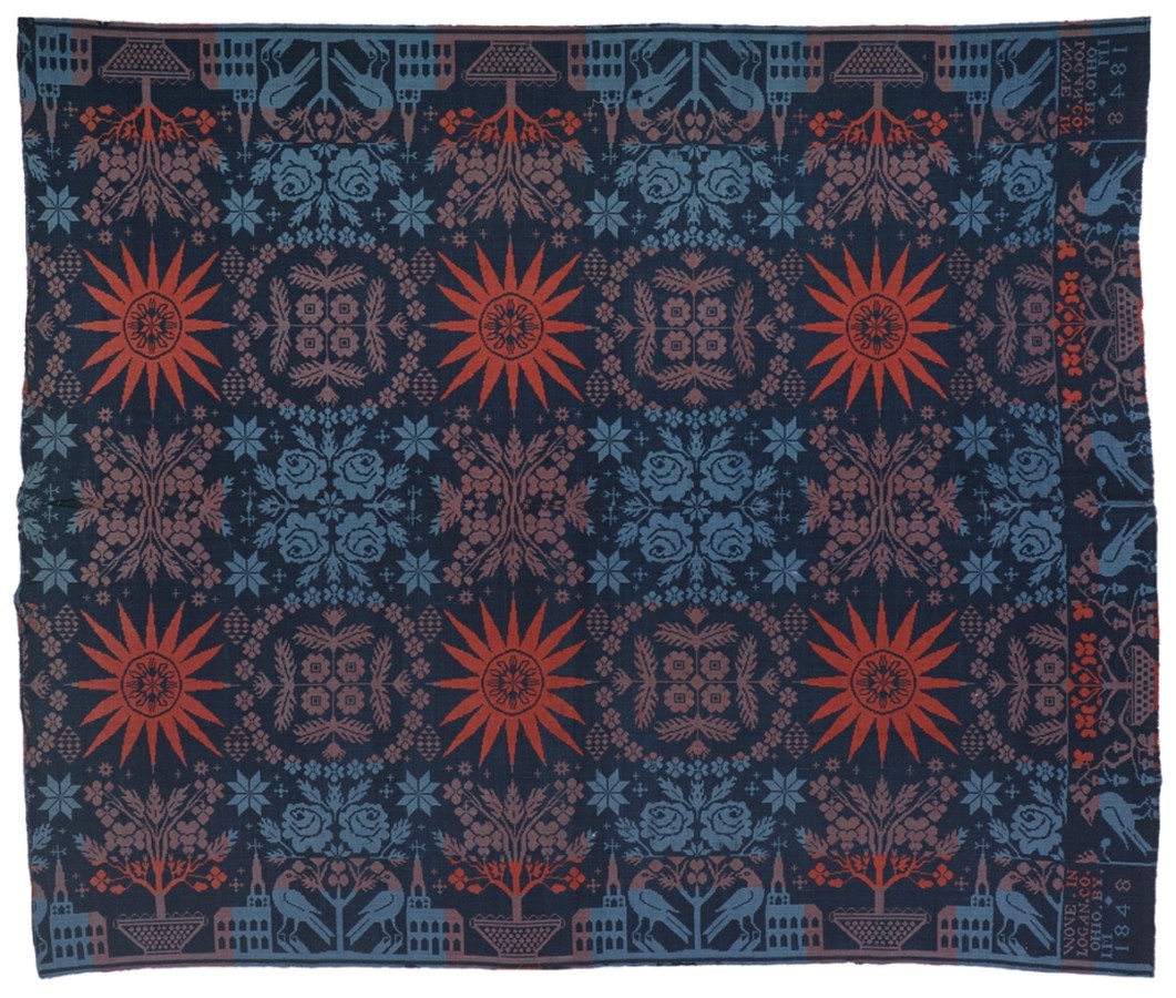 This coverlet is symmetrical with a dark blue background and red, light red and light blue motifs. The pattern includes a church, starbursts, florals, and curvilinear designs.